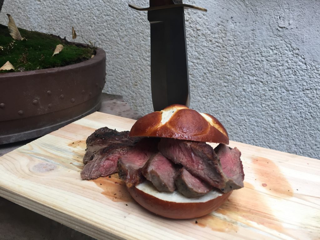 Ein Laugenbrötchen das mit einem Rumpfsteak belegt ist. das Rumpfsteak wurde auf 54 Grad Kerntemperatur gegrillt.